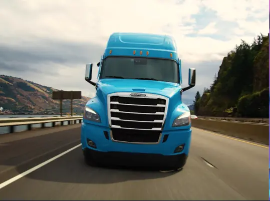 A blue truck with detailed 3D texturing driving on a road, focusing on the front grille.