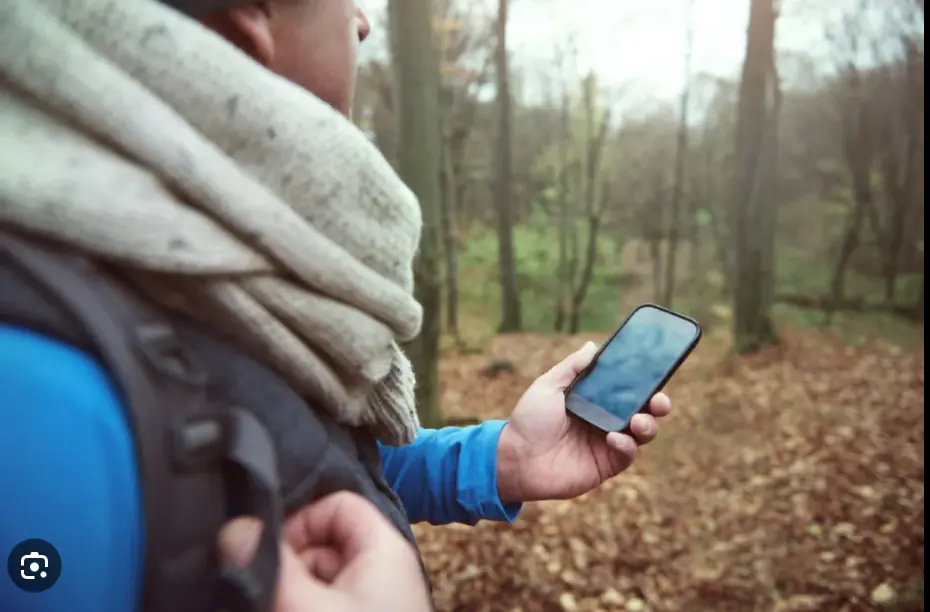 Person using a mobile phone outdoors during an adventure in a forest, showcasing lifestyle photography.